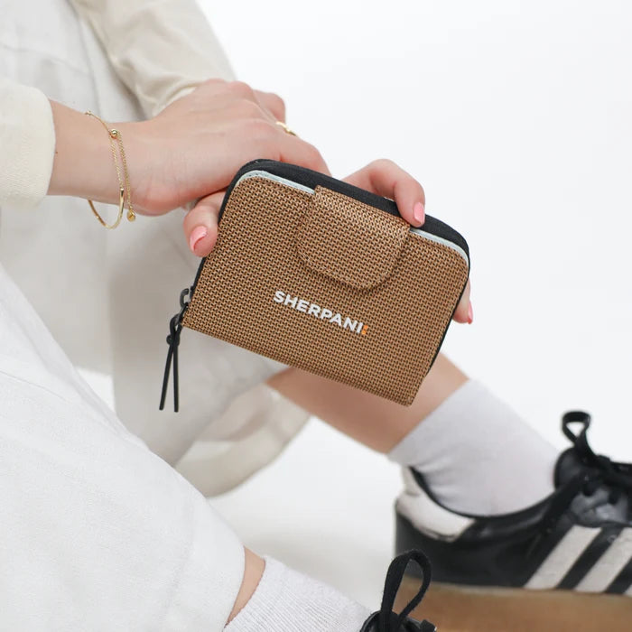 Woman holding a Sherpani Barcelona Sand Anti-Theft Mini Wallet on white backdrop.  #color_sand-tan