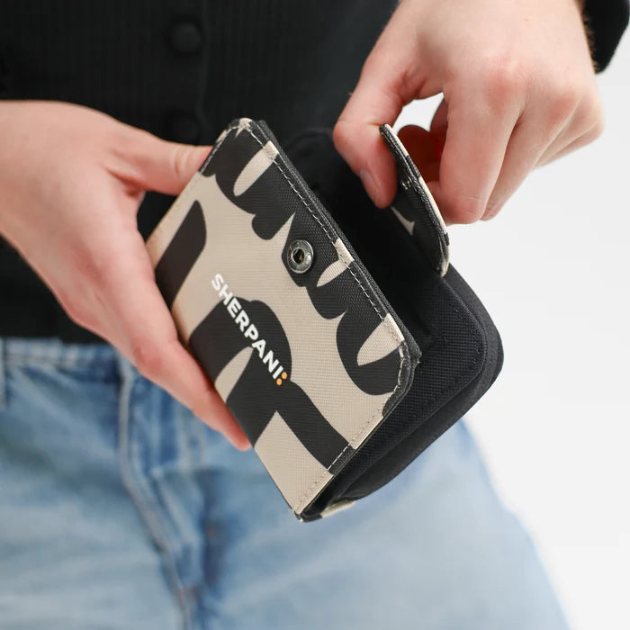 Woman opening a Sherpani Barcelona Ciao RFID Mini Wallet on white backdrop.  #color_ciao-print