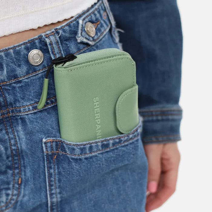 A Sherpani Barcelona Olivine RFID Mini Wallet in a front jean pocket on white backdrop.  #color_olivine-green