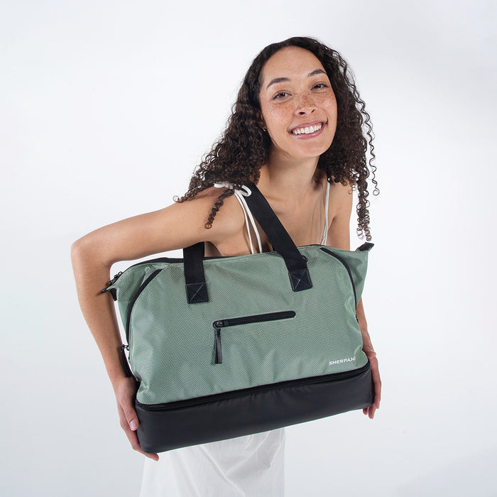 A woman holding a Sherpani Boston Aloe Mist Green Anti-theft Weekender against a white background. #color_aloe-mist-green