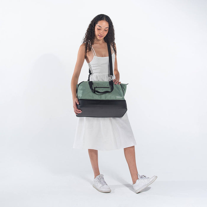 A woman wearing a Sherpani Boston Aloe Mist Green Anti-theft Weekender by crossbody strap against a white background. #color_aloe-mist-green