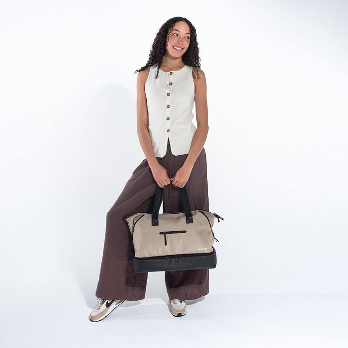 A woman holding a Sherpani Boston Straw Beige Anti-theft Weekender against a white background. #color_straw-beige