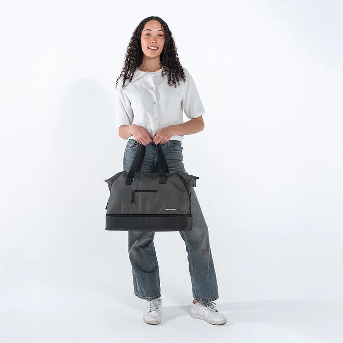 A woman holding a Sherpani Boston Granite Anti-theft Weekender against a white background. #color_granite-grey