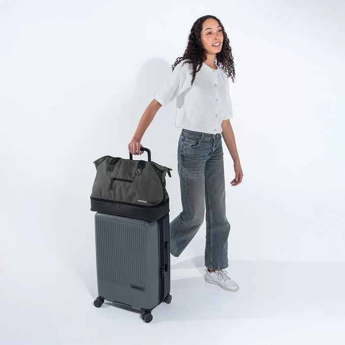 Woman holds Sherpani Boston Granite Anti-theft Weekender on Sherpani Meridian Granite Carry-On on a white backdrop. #color_granite-grey