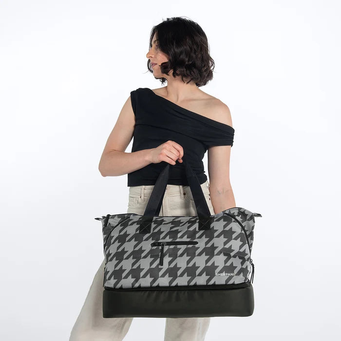 A woman holding a Sherpani Boston Houndstooth Anti-theft Weekender against a white background. #color_houndstooth-print