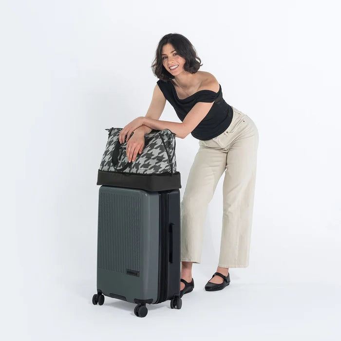 Woman holds Sherpani Boston Houndstooth Anti-theft Weekender on Sherpani Meridian Granite Carry-On on a white backdrop. #color_houndstooth-print
