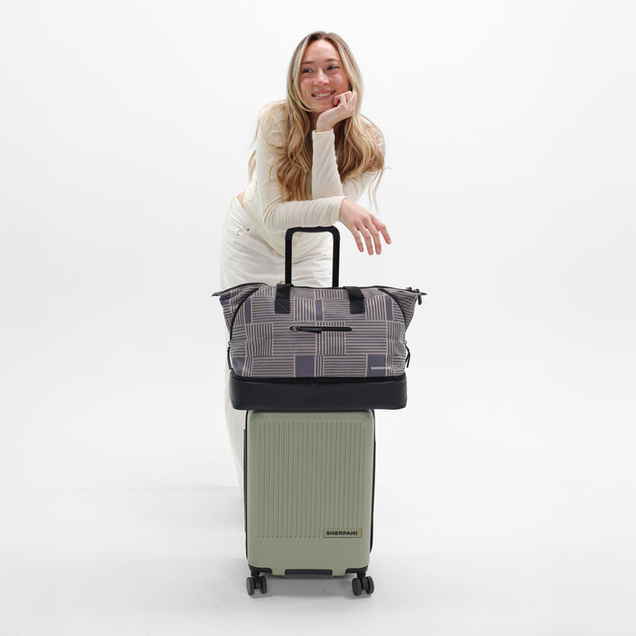 Woman holds Sherpani Boston Passport Anti-theft Weekender on Sherpani Meridian Matcha Carry-On on a white backdrop. #color_passport-print