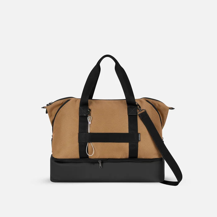 A Sherpani Boston Sand Anti-theft Weekender, back view showing luggage strap & strap options on white backdrop.  #color_sand-tan