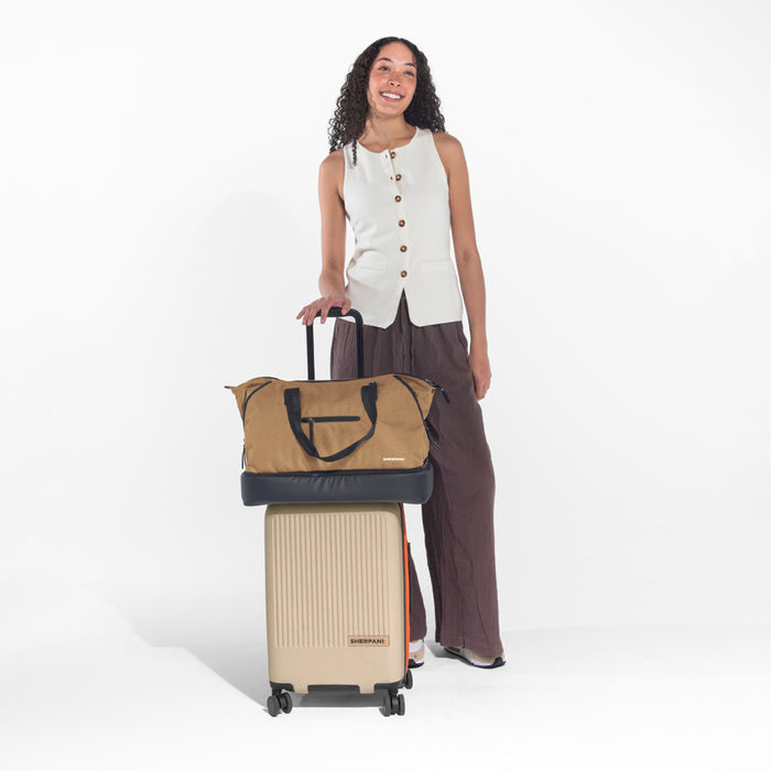 Woman holds Sherpani Boston Sand Anti-theft Weekender on Sherpani Meridian Chai Carry-On on a white backdrop. #color_sand-tan