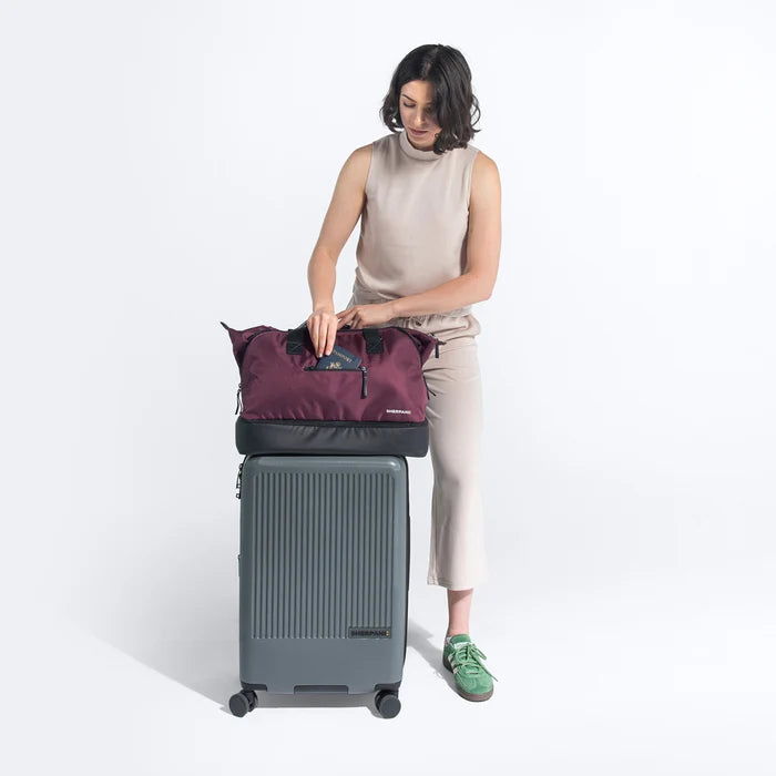 Woman holds Sherpani Boston Smoky Orchid Anti-theft Weekender on Sherpani Meridian Granite Carry-On on a white backdrop. #color_smoky-orchid-pink