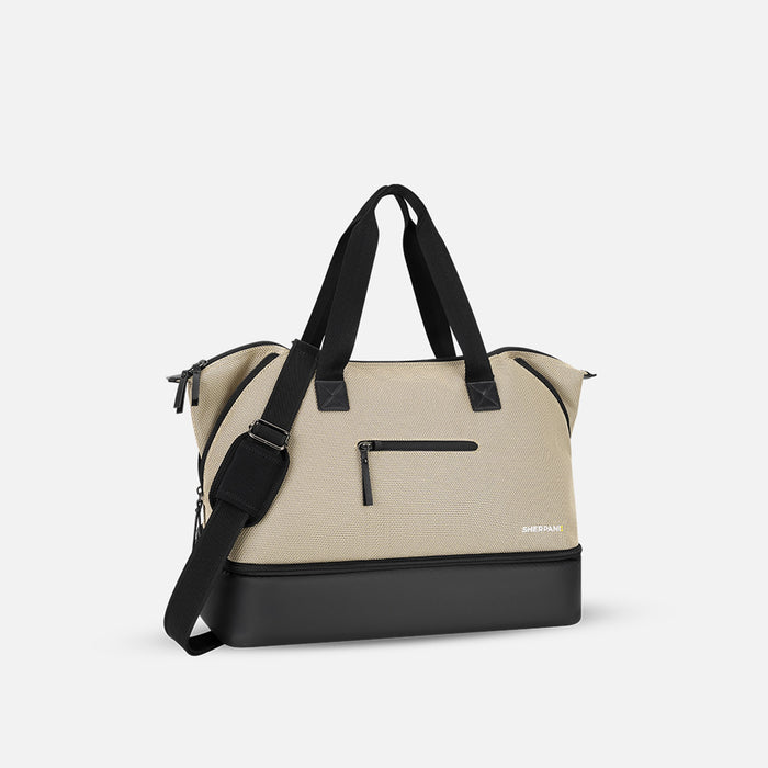 A Sherpani Boston Straw Beige Anti-theft Weekender, 3/4 view showing strap and lockable pocket on white background. #color_straw-beige