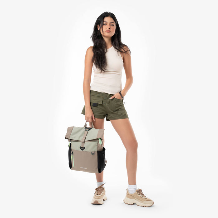Woman holding a Sherpani Cabo Desert Rose Day Pack by the top strap against a white background. #color_desert-aloe