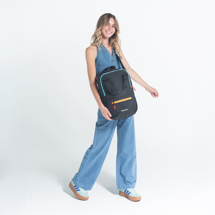 Woman wearing a Sherpani Camden Chromatic Black Backpack across her shoulder against white background.  #color_chromatic-black