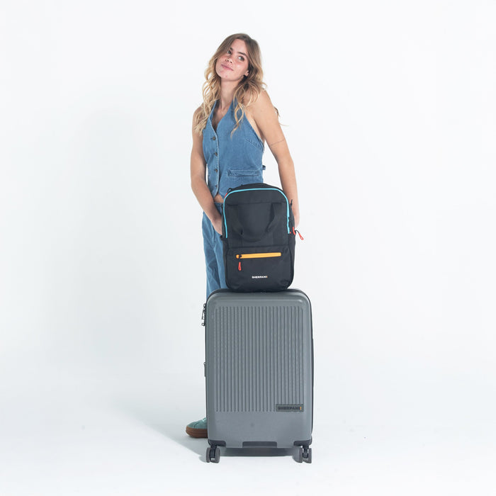 Woman holding a Sherpani Camden Chromatic Black Backpack on top Sherpani Meridian Granite luggage on white background.   #color_chromatic-black