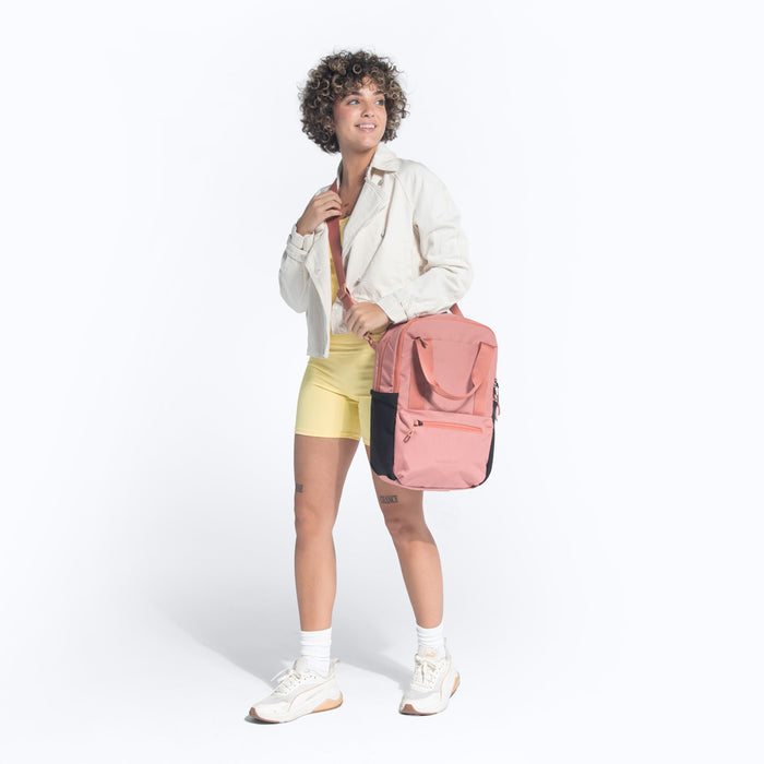 Woman wearing a Sherpani Camden Desert Pink Backpack across her shoulder against white background.   #color_desert-pink