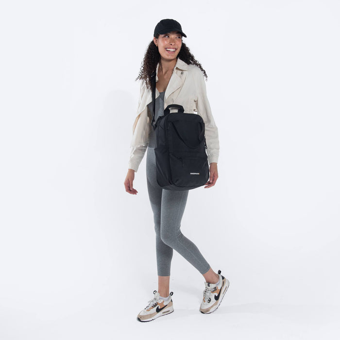 Woman wearing a Sherpani Camden Raven Black Backpack across her shoulder against white background. #color_raven-black