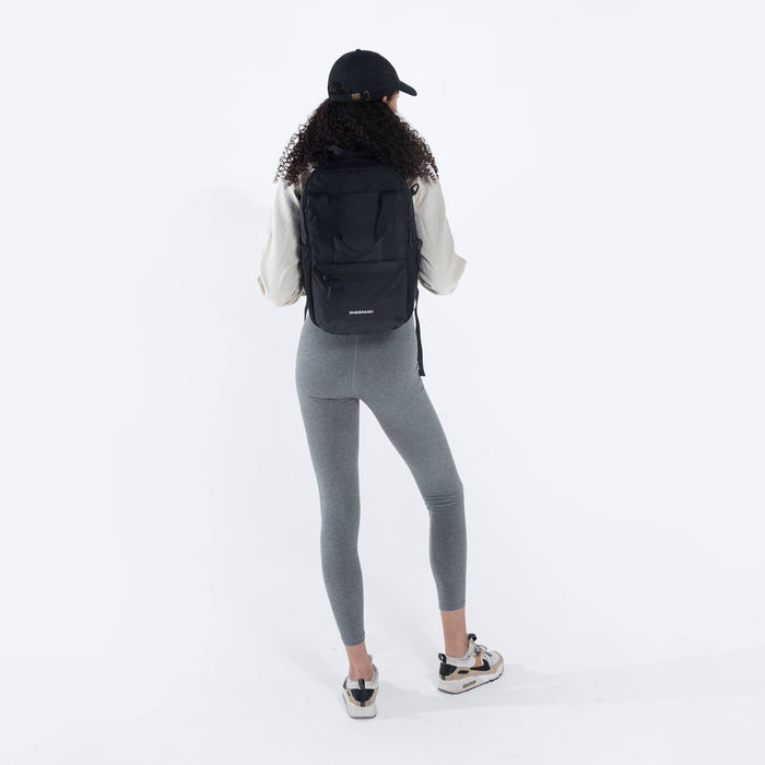 Woman wearing a Sherpani Camden Raven Black Backpack on her back against white background. #color_raven-black