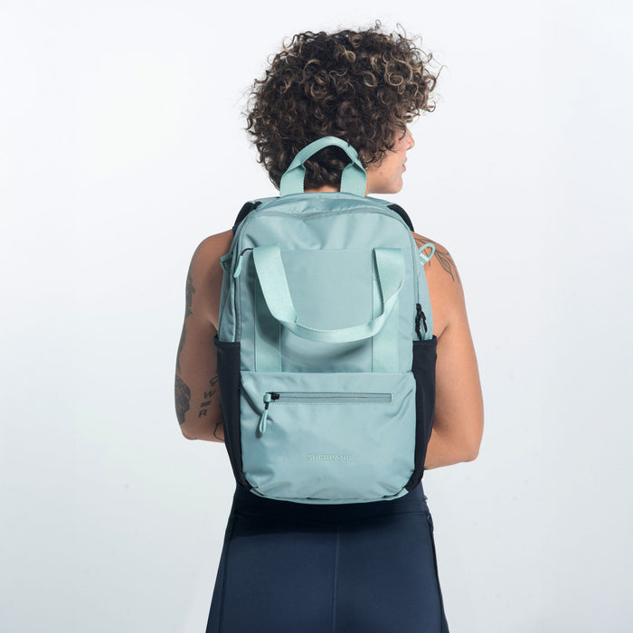 Woman wearing a Sherpani Camden Surf Blue Backpack on her back against white background.  #color_surf-blue