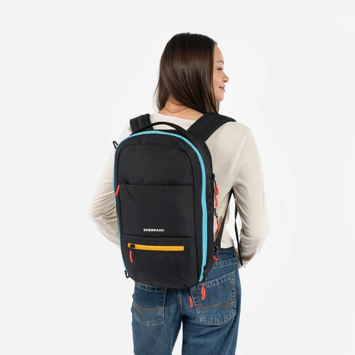 A woman wearing a Sherpani Camden Chromatic Black Ultimate Backpack on her back against white background.  #color_chromatic-black