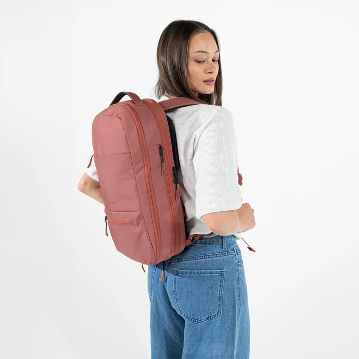 A woman wearing a Sherpani Camden Desert Pink Ultimate Backpack on her back against white background.  #color_desert-pink