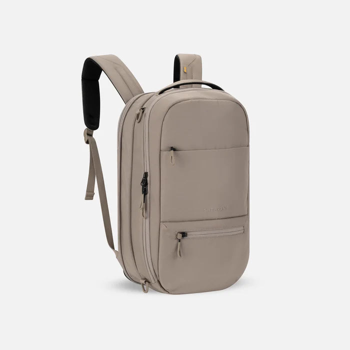 A Sherpani Camden Dune Ultimate Backpack, 3/4 view showing unzipped extender and strap options on white backdrop. #color_dune-tan
