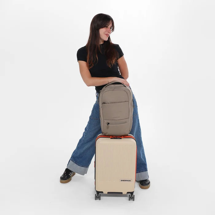 Woman holding a Sherpani Camden Dune Ultimate Backpack on top of Sherpani Meridian Chai luggage on white background.  #color_dune-tan