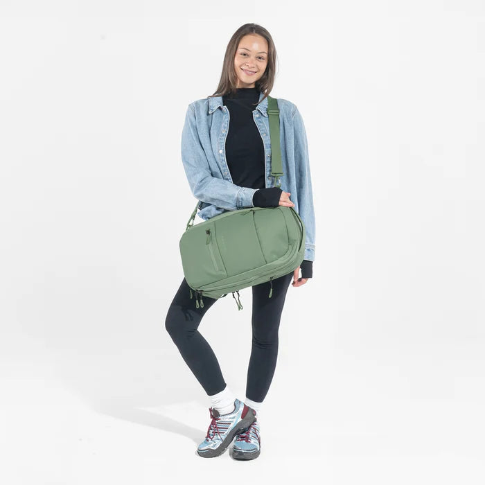 A woman wearing a Sherpani Camden Olivine Ultimate Backpack with crossbody strap against white background #color_olivine-green