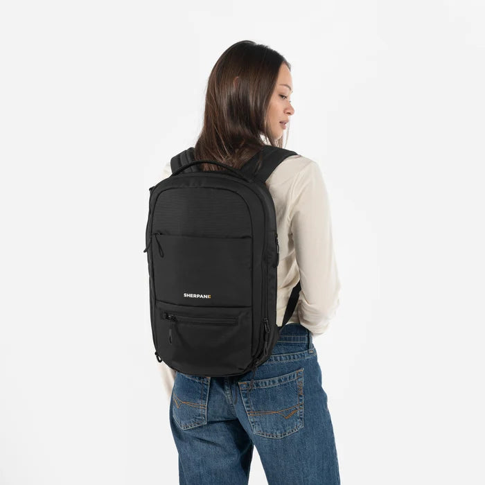 A Woman wearing a Sherpani Camden Raven Black Ultimate Backpack on her back against white background. #color_raven-black