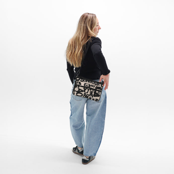A woman wearing a Sherpani Ceara Ciao Expandable Crossbody on her shoulder against a white background.   #color_ciao-print
