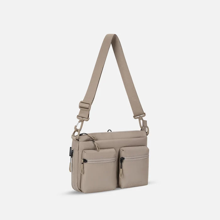 A Sherpani Ceara Dune Expandable Crossbody, 3/4 view showing two front pockets and the closed expandable pocket on a white background.    #color_dune-tan