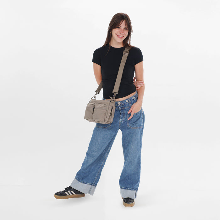 A woman wearing a Sherpani Ceara Dune Expandable Crossbody on her shoulder against a white background. #color_dune-tan