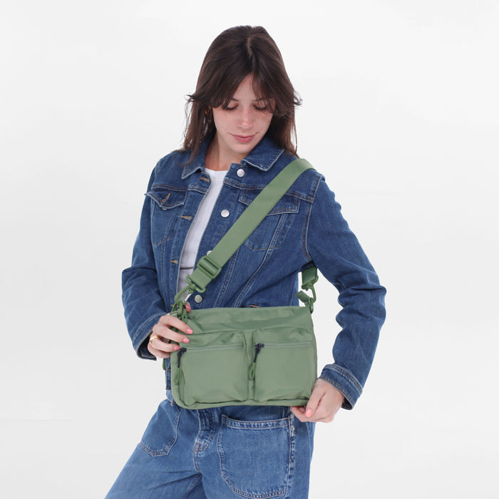 A woman wearing a Sherpani Ceara Olivine Expandable Crossbody on her shoulder against a white background.   #color_olivine-green