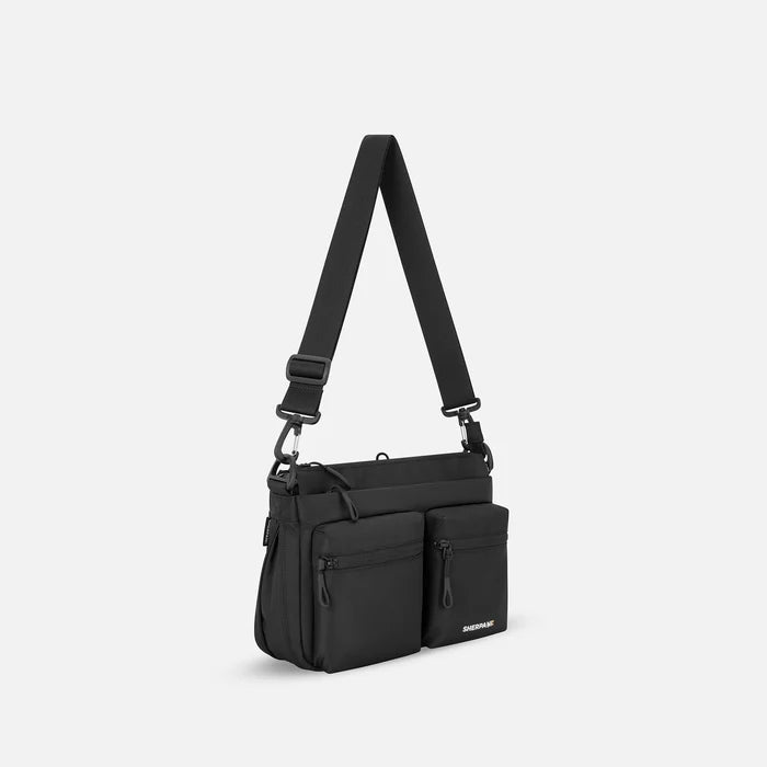 A Sherpani Ceara Raven Black Expandable Crossbody, 3/4 view showing two front pockets and the open expandable pocket on a white background.   #color_raven-black