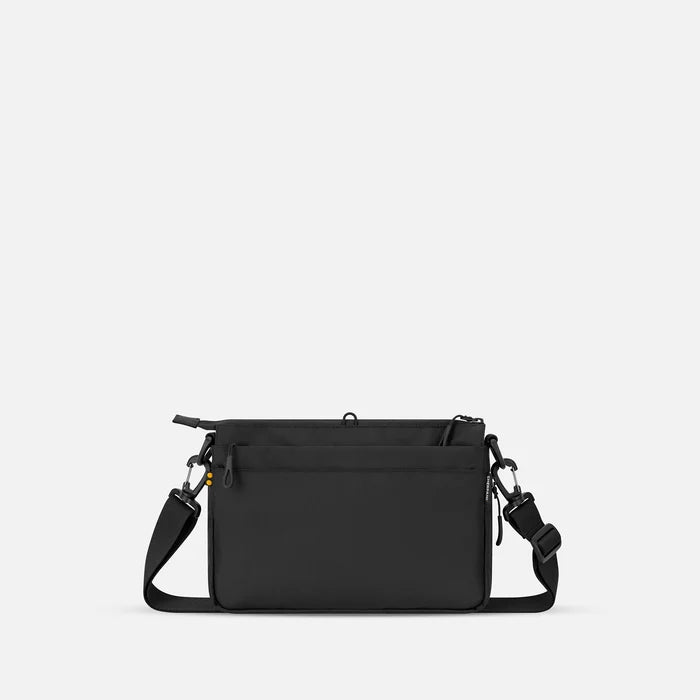 A Sherpani Ceara Raven Black Expandable Crossbody, back view showing the back pocket on a white background.  #color_raven-black
