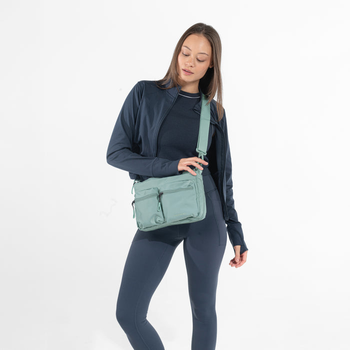 A woman wearing a Sherpani Ceara Surf Blue Expandable Crossbody on her shoulder against a white background.   #color_surf-blue