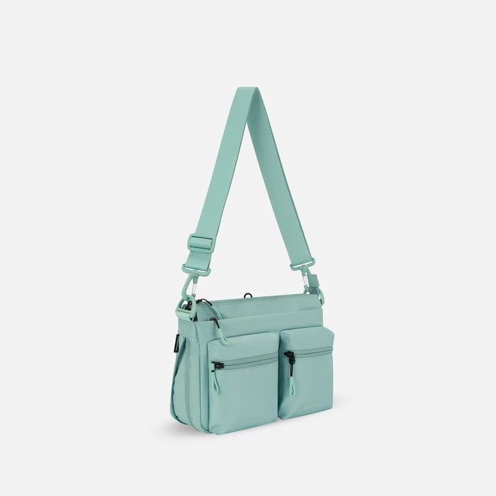A Sherpani Ceara Surf Blue Expandable Crossbody, 3/4 view showing two front pockets and the open expandable pocket on a white background.  #color_surf-blue