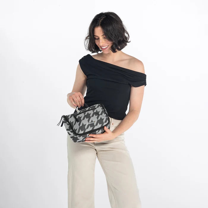 Woman holding a Sherpani Co-Pilot Houndstooth Travel Toiletry Case against white backdrop. #color_houndstooth-print