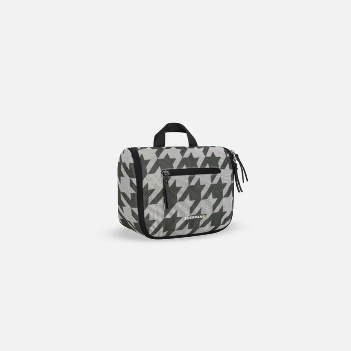 A Sherpani Co-Pilot Houndstooth Travel Toiletry Case, 3/4 view showing handheld strap and zipper pockets on white backdrop. #color_houndstooth-print