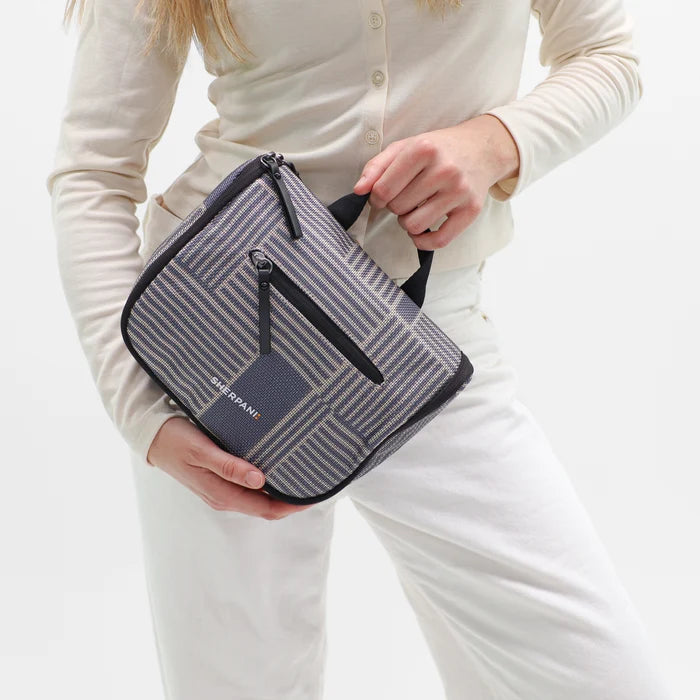 Woman holding a Sherpani Co-Pilot passport Travel Toiletry Case against white backdrop. #color_passport-print