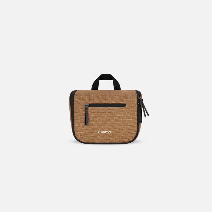 A Sherpani Co-Pilot Sand Travel Toiletry Case, front view showing handheld strap and zipper pockets on white backdrop. #color_sand-tan