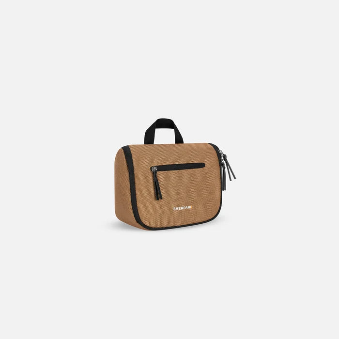 A Sherpani Co-Pilot Sand Travel Toiletry Case, 3/4 view showing handheld strap and zipper pockets on white backdrop. #color_sand-tan