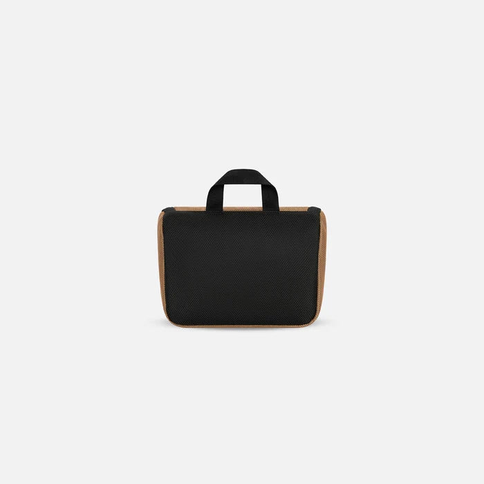 A Sherpani Co-Pilot Sand Travel Toiletry Case, back view showing black backside on white backdrop. #color_sand-tan