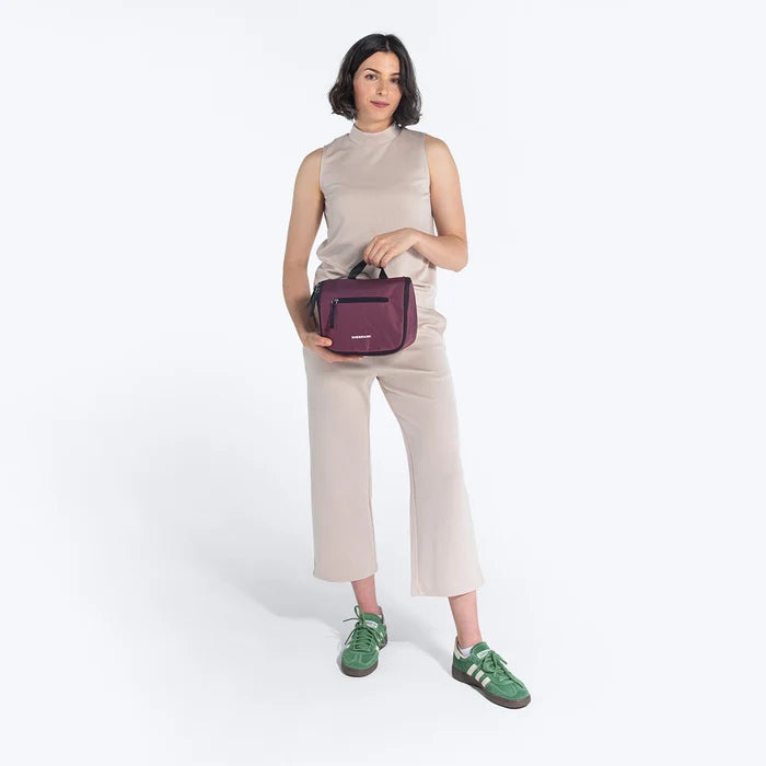 Woman holding a Sherpani Co-Pilot Smoky Orchid Travel Toiletry Case against white backdrop. #color_smoky-orchid-pink