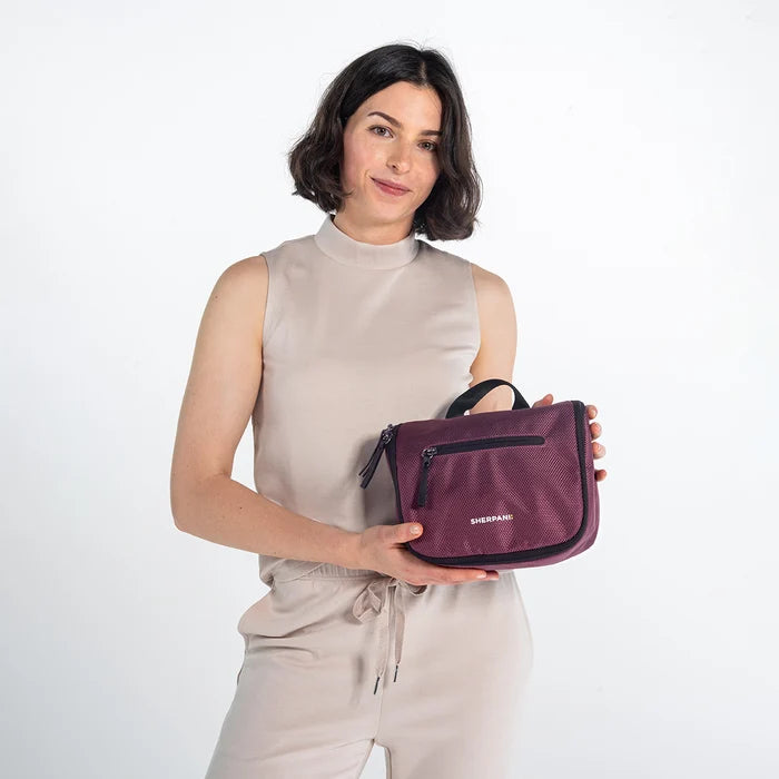 Woman holding a Sherpani Co-Pilot Smoky Orchid Travel Toiletry Case against white backdrop. #color_smoky-orchid-pink