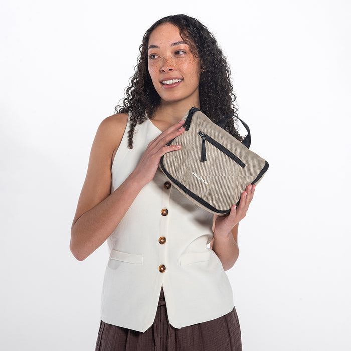 Woman holding a Sherpani Co-Pilot Straw Beige Travel Toiletry Case against white backdrop. #color_straw-beige