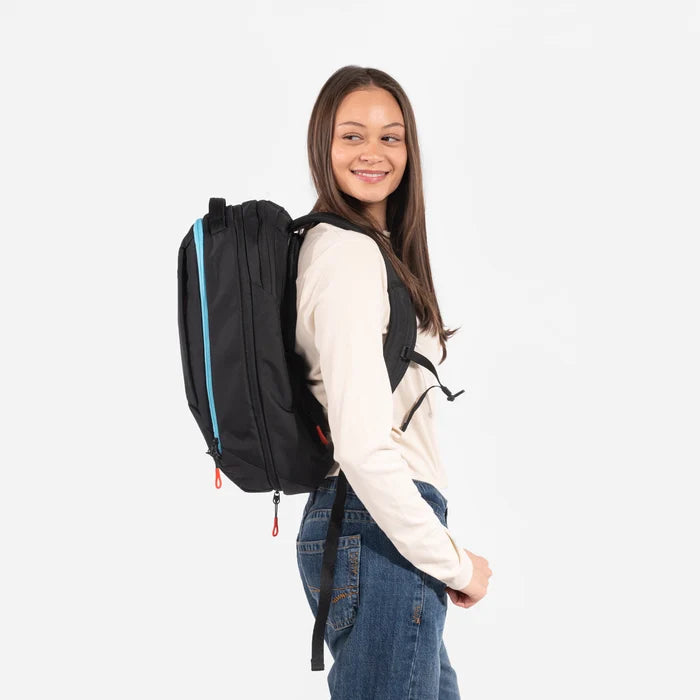 A woman wearing a Sherpani Crew Chromatic Black Travel Backpack on her back against a white background. #color_chromatic-black