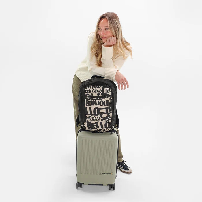 A woman holding a Sherpani Crew Ciao Travel Backpack on top of a Sherpani Meridian Luggage against a white background. #color_ciao-print