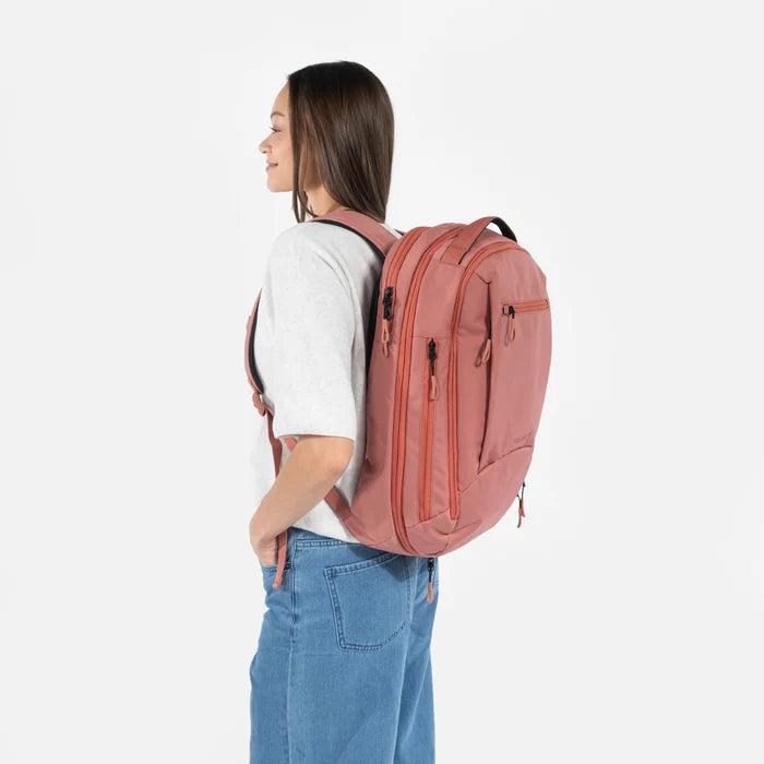 A woman wearing a Sherpani Crew Desert Pink Travel Backpack on her back against a white background.  #color_desert-pink