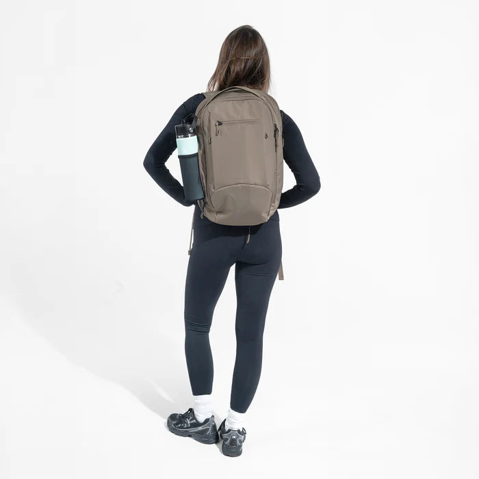 A woman wearing a Sherpani Crew Dune Backpack on her back against a white background. #color_dune-tan