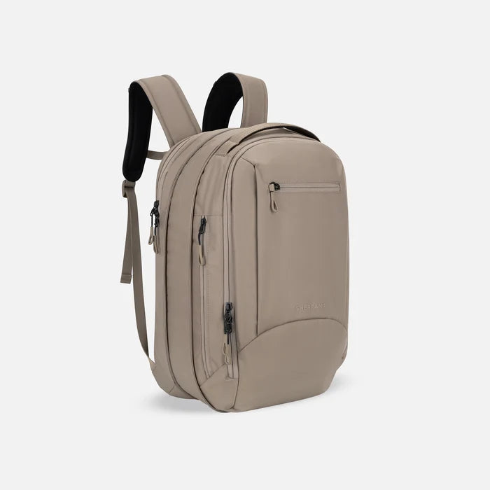 A Sherpani Crew Dune Travel Backpack, 3/4 view showing lockable zippers and the extender pocket against a white background #color_dune-tan